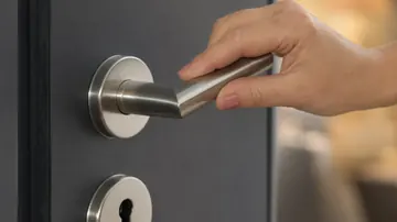 Main abaissant la poignée en inox d'une porte d'appartement